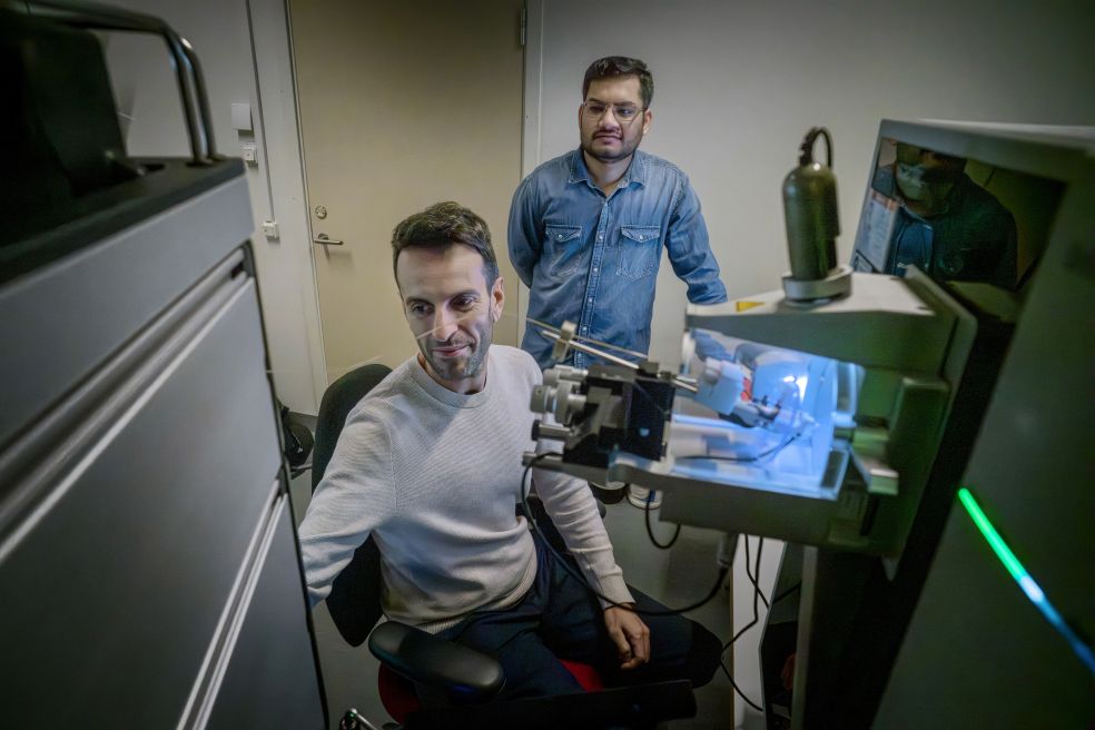 Två män i ett laboratorium; en sitter vid en maskin och den andra står bakom.