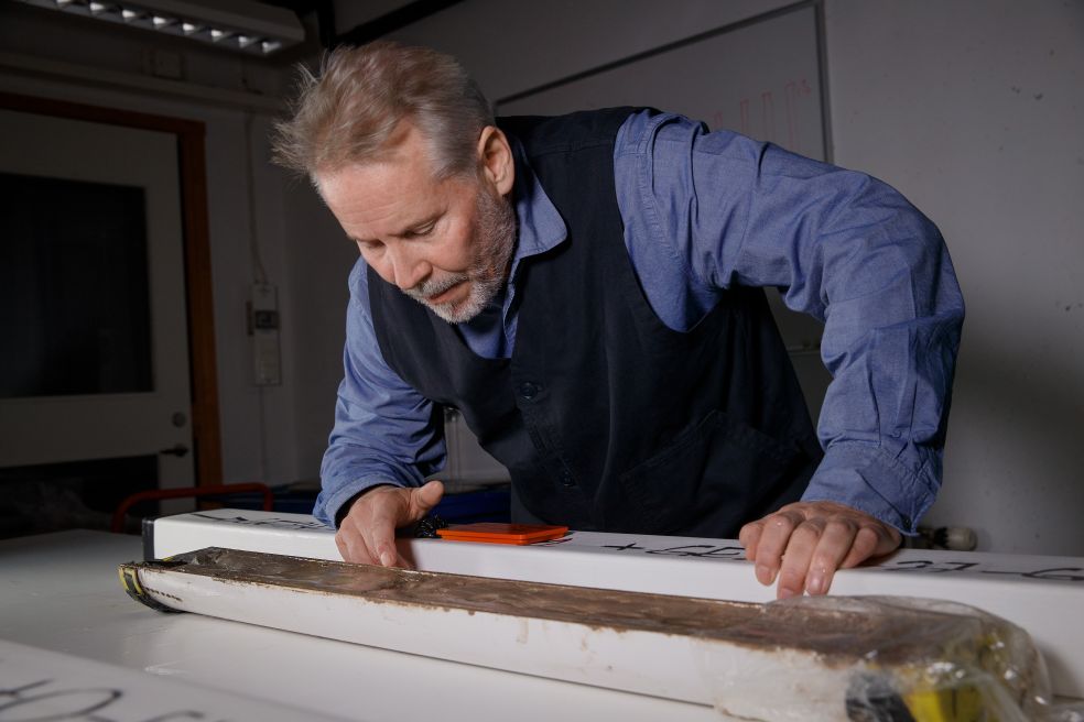 En man inspekterar noggrant en lång föremål på ett bord i ett laboratoriemiljö.