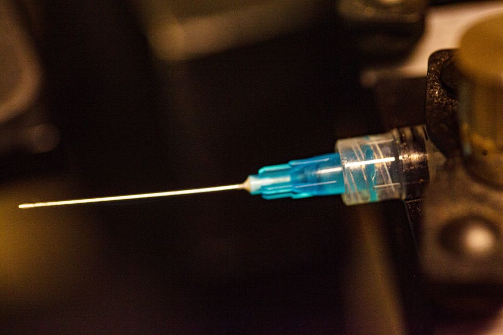 Blå spruta med nål, fokuserad på spetsen, mot mörk bakgrund.