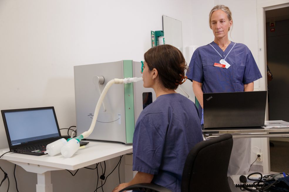 En patient sitter vid skrivbordet med en medicinsk apparat, övervakad av en läkare.