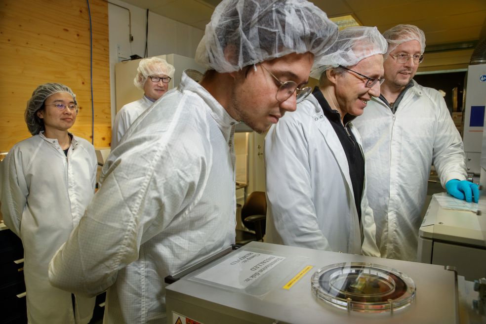 Flera personer i labbrockar och hårnät observerar en apparat.