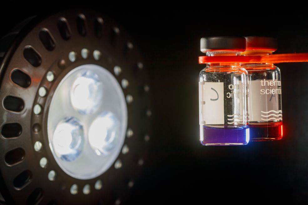 Två genomskinliga flaskor med färgglada vätskor sväva framför en lampa med tre ljuskällor.