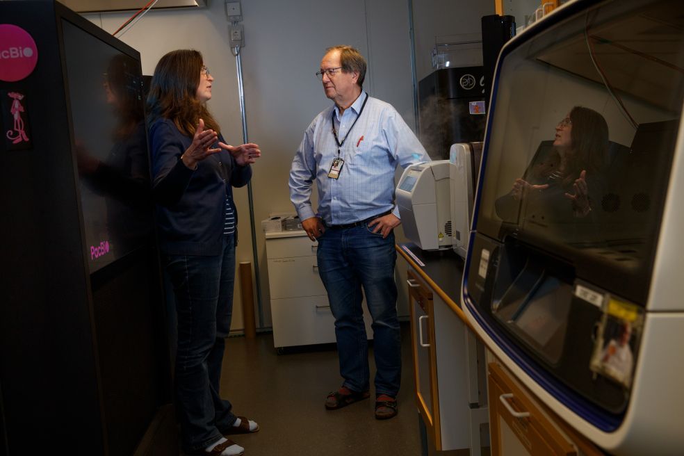 Två personer diskuterar vid en laboratoriemiljö med utrustning runtom.