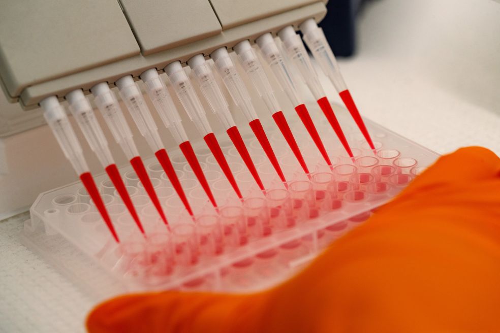 Pipetter med röd vätska i provrör, hand med orange handske i fokus.
