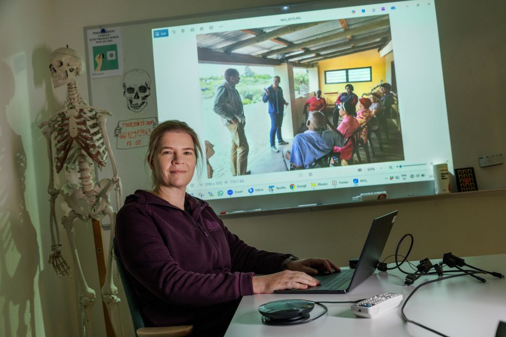 Kvinna vid laptop i klassrum, skärm med presentation och publiken i bakgrunden.