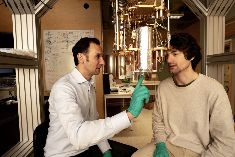 Två män i labbmiljö diskuterar vid en avancerad vetenskaplig apparat.