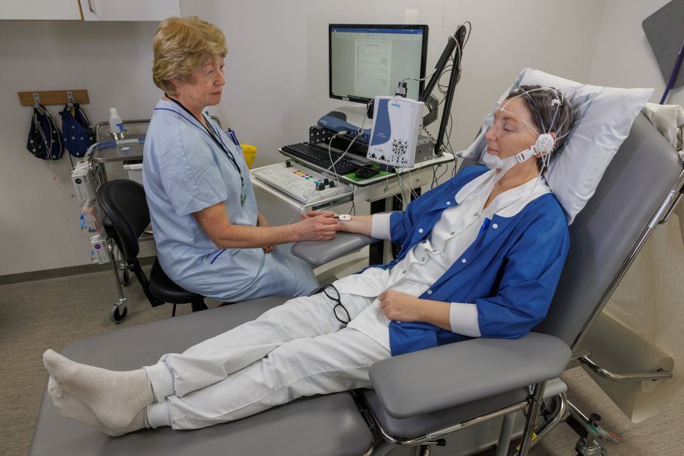 Sjuksköterska sitter bredvid patient med medicinteknisk utrustning i en klinik.