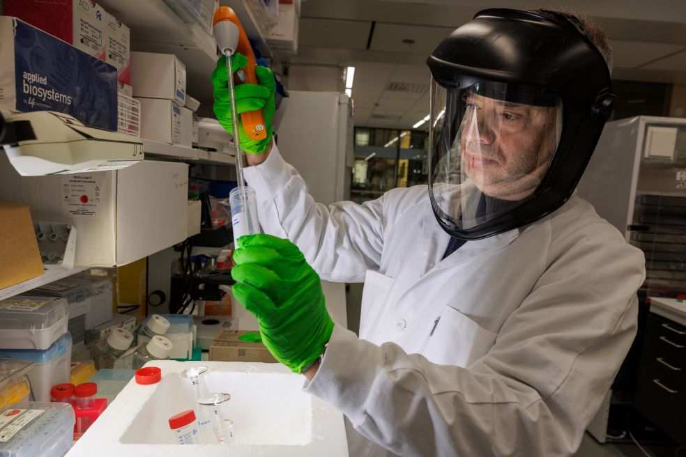 Forskningslaboratoriemiljö med en person i skyddsutrustning som hanterar ett provrör.