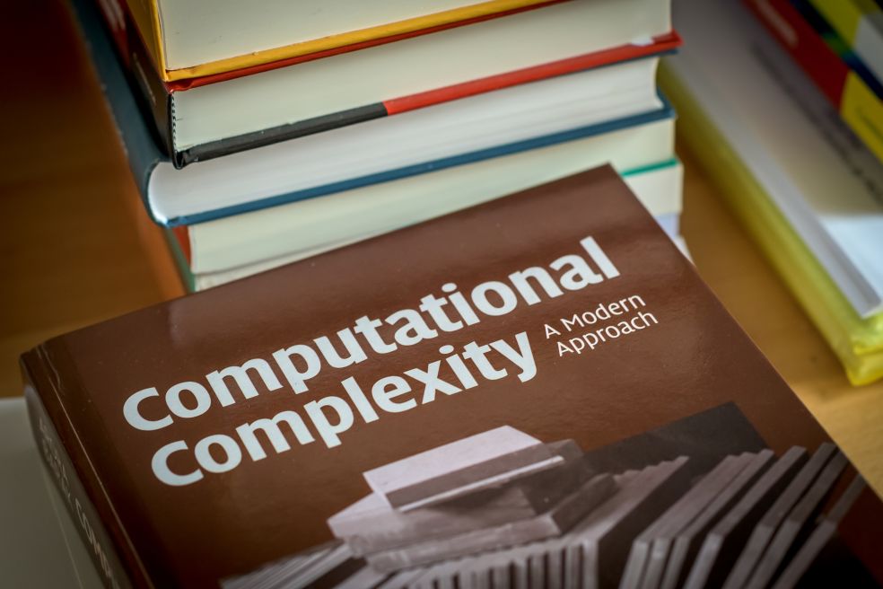 Bok med titeln "Computational Complexity" ligger på ett bord bland andra böcker.