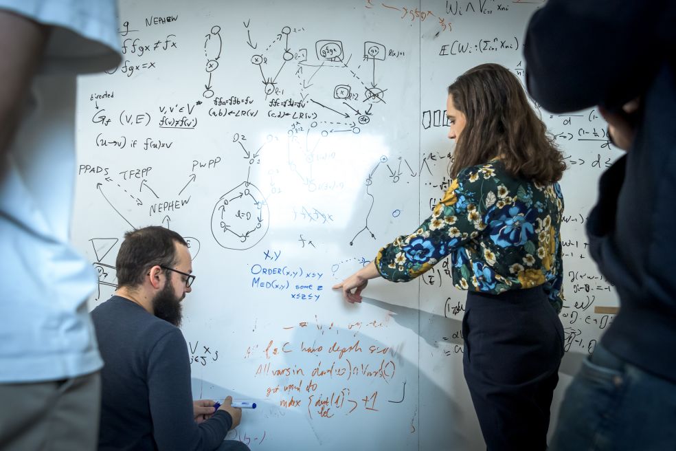 Två personer arbetar tillsammans vid en skrivtavla med matematiska formler och diagram.