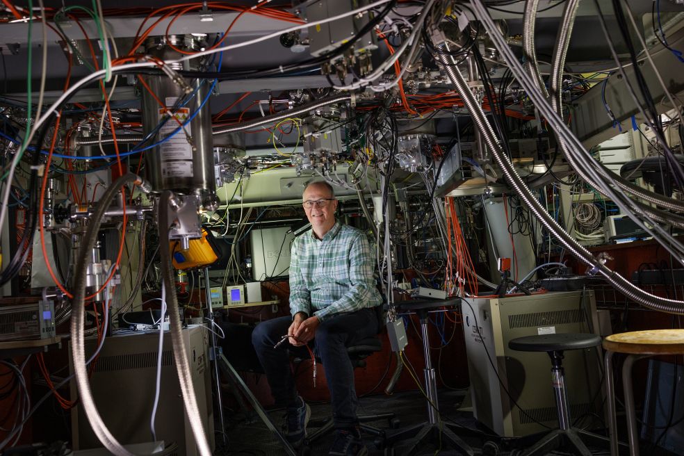 En man sitter bland komplexa kablar och utrustning i en teknisk miljö.