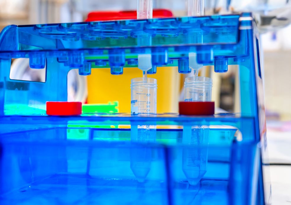 Blå laboratorieutrustning med rör och färgade lock i en vit miljö.