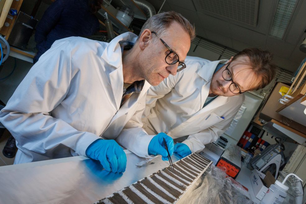 Två forskare i vita labbrockar inspekterar ett experiment i ett laboratorium.