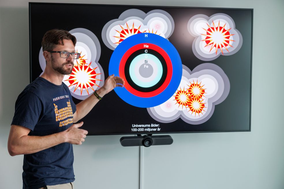 Man pekar på en färgglad graf på en stor skärm i en ljus lokal.