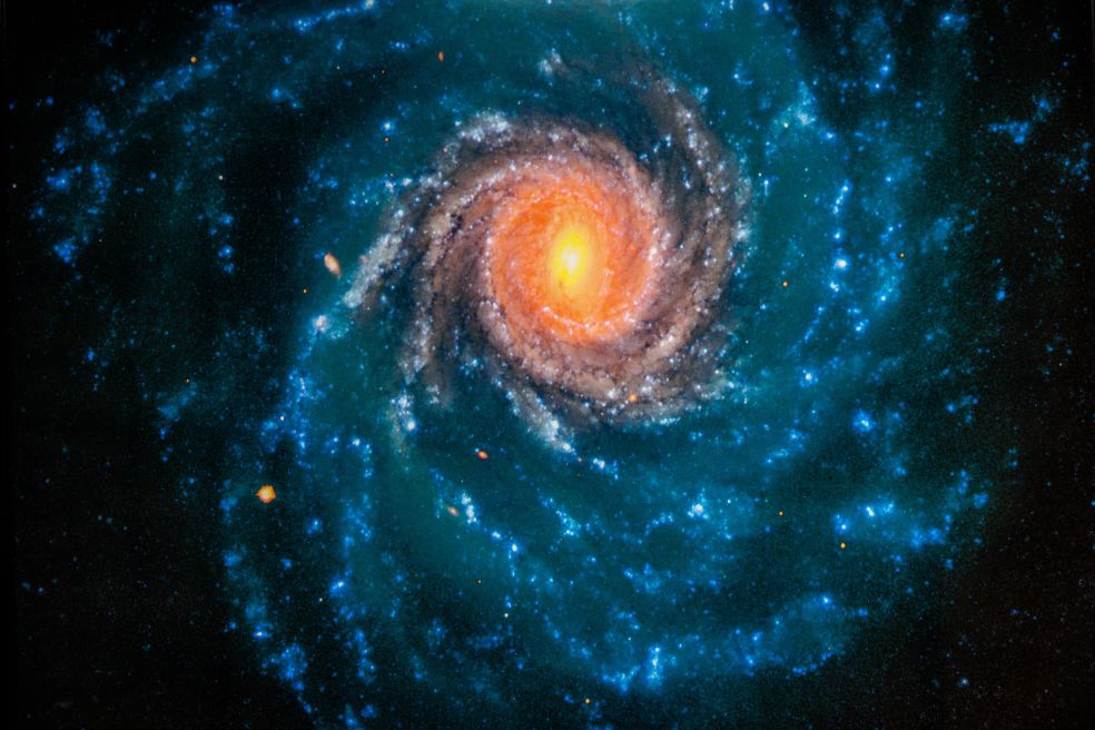 En färgglad spiralgalax med en ljus kärna i mitten och blåa stjärnor runt.