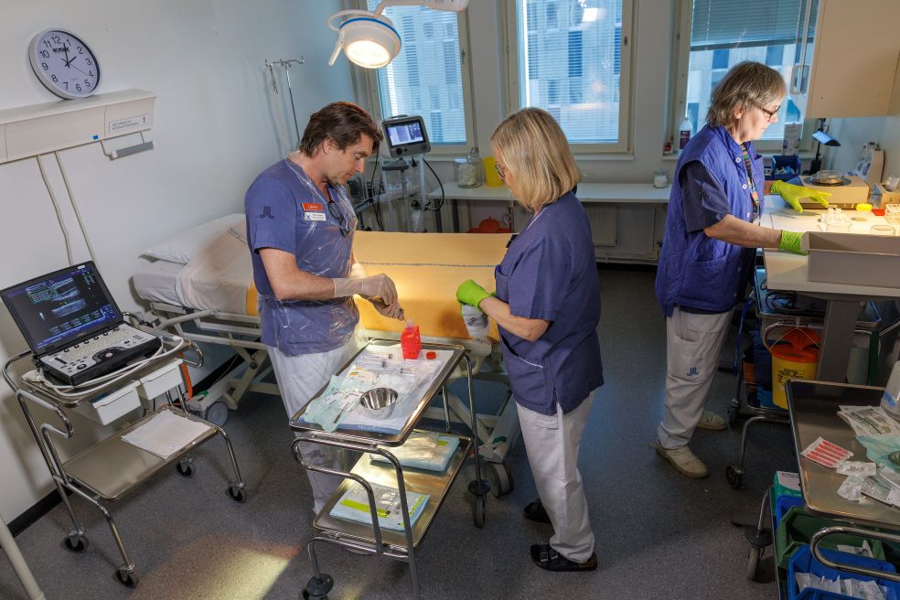 Tre sjukvårdspersonal arbetar tillsammans i ett modernt sjukhusrum.