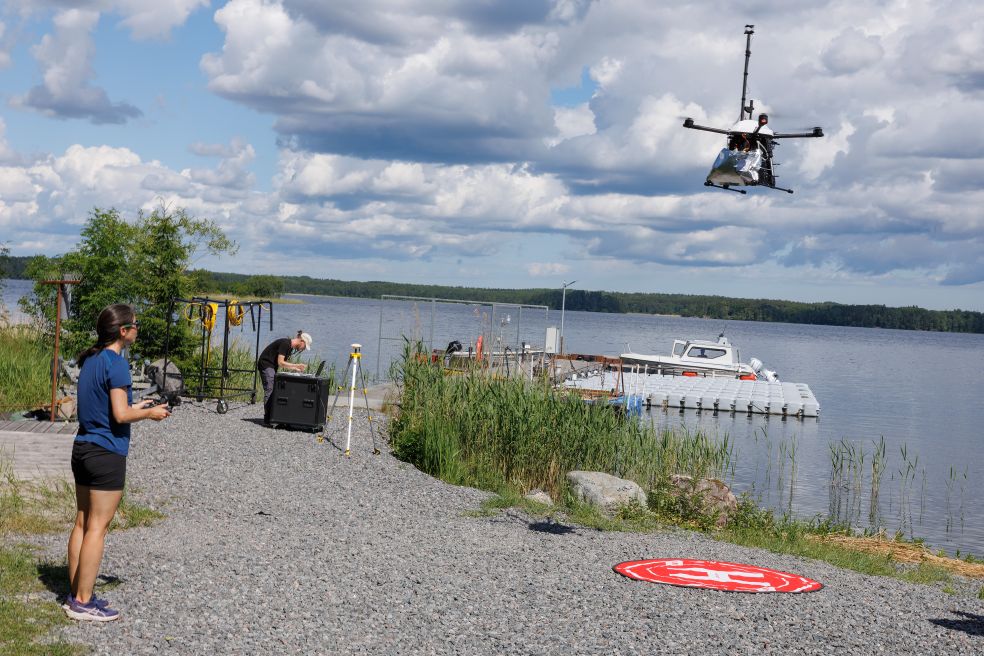 En person styr en drönare över en sjö med molnig himmel i bakgrunden.