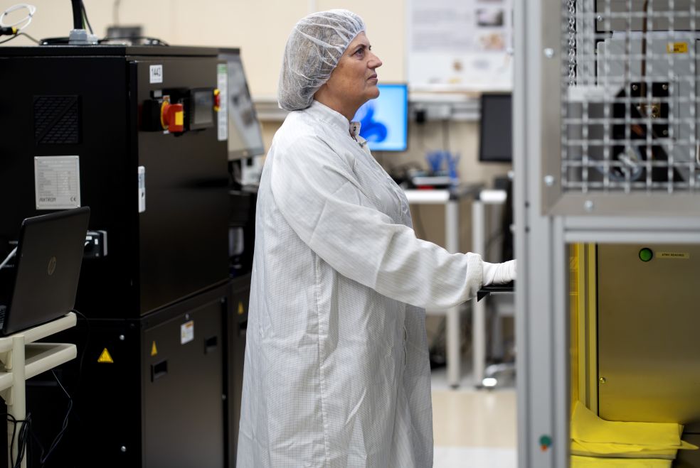 En person i skyddskläder står vid en maskin i ett laboratoriemiljö.
