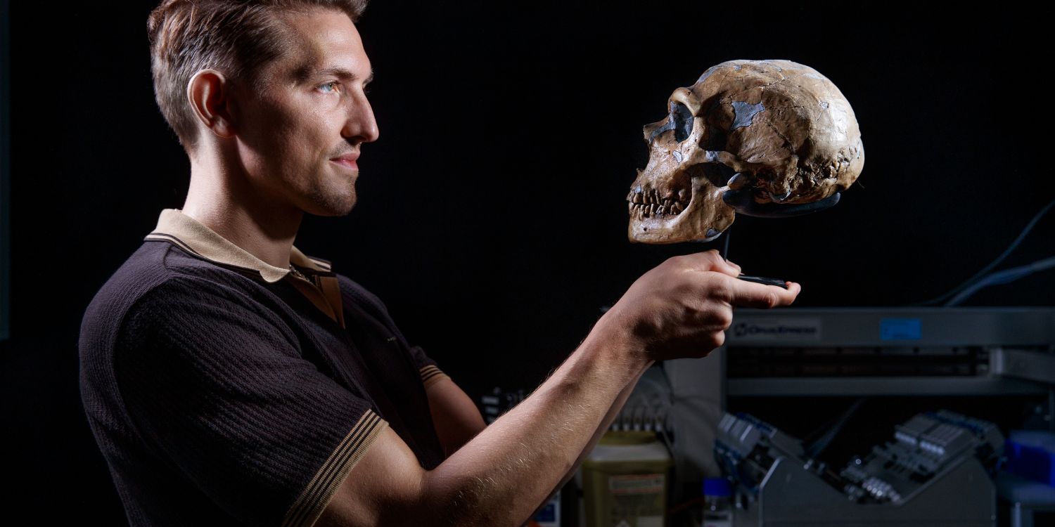 En man som håller en mänsklig skalle i en laboratoriemiljö.