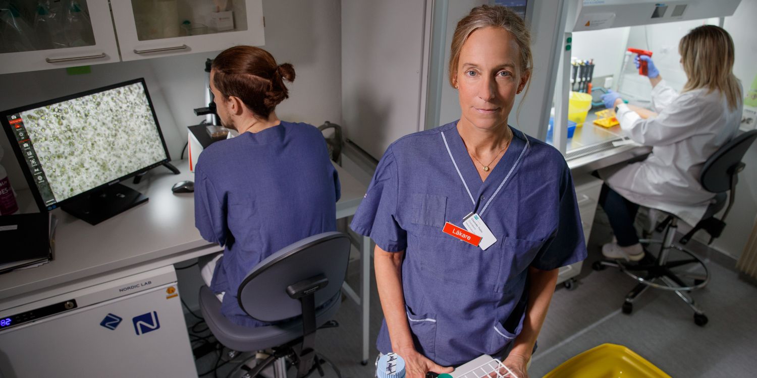 Kvinna i laboratoriemiljö håller en provplatta, andra forskare arbetar i bakgrunden.