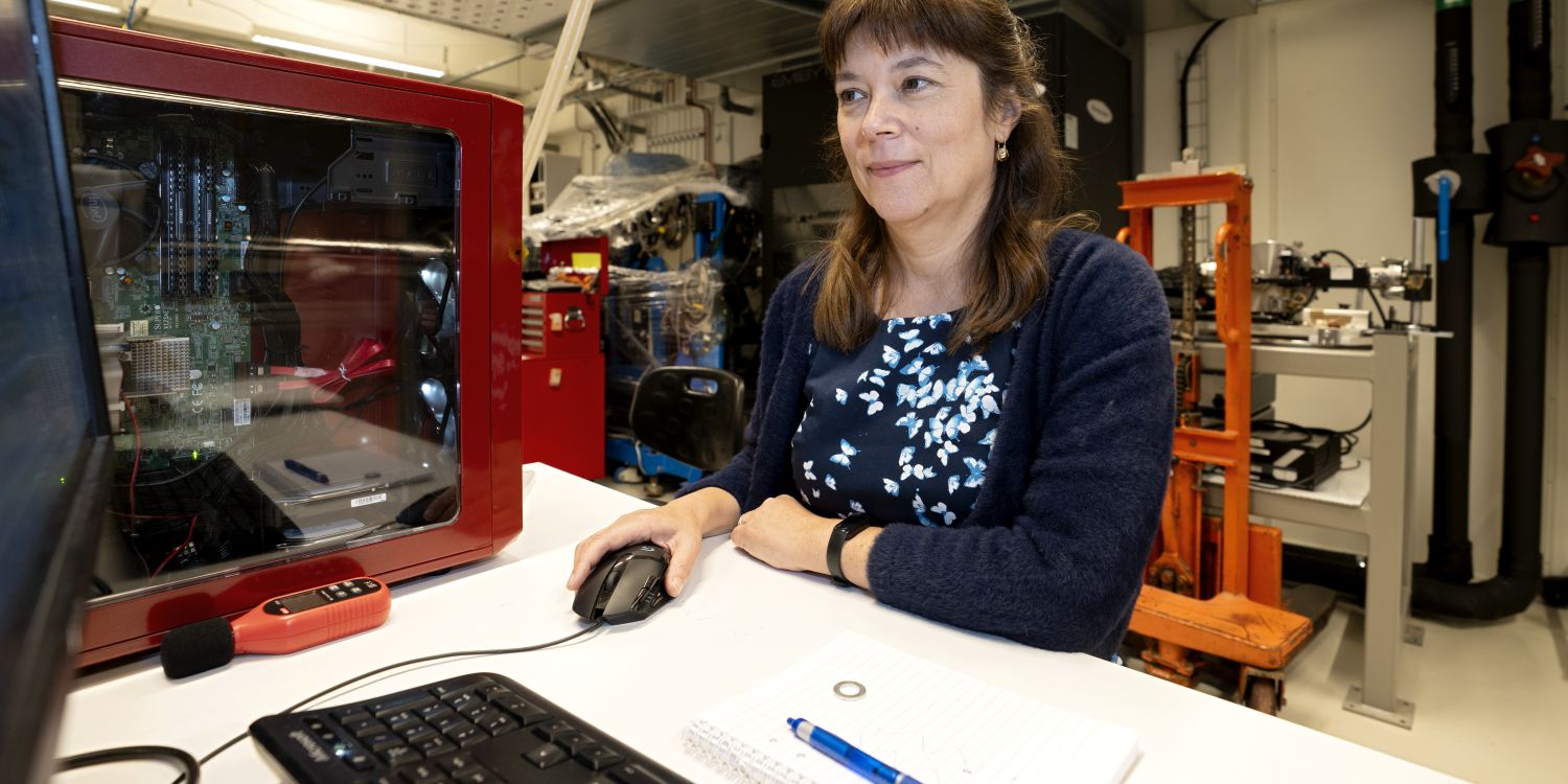 Kvinna sitter vid ett skrivbord framför en dator, omgiven av teknisk utrustning.