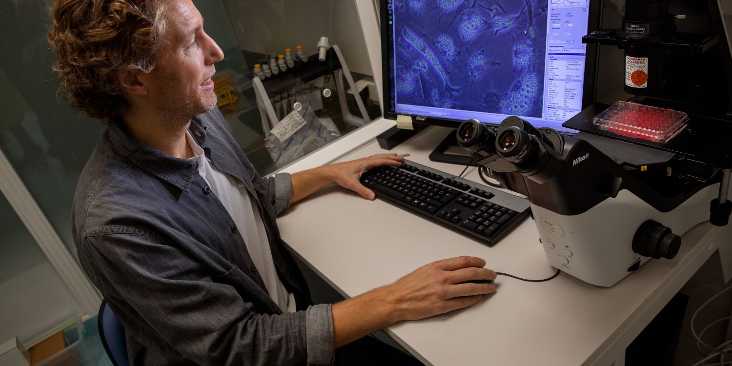 Man i laboratorium arbetar vid en dator med mikroskop och prover i bakgrunden.