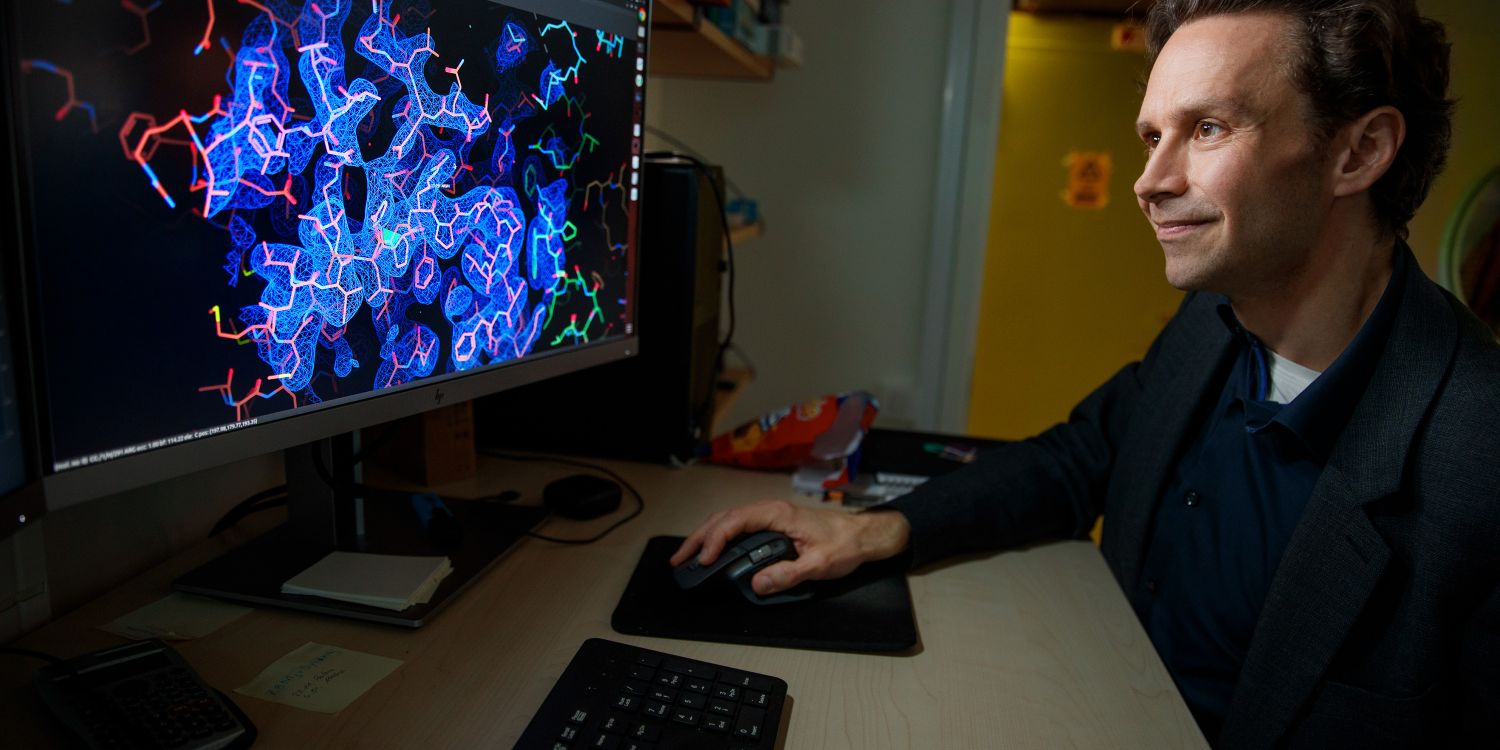 En man arbetar vid en dator med en färgglad molekylärstruktur på skärmen.