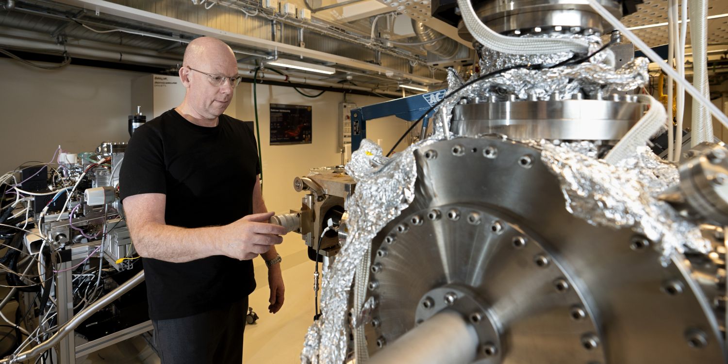 Forskare inspekterar en stor maskin i ett laboratorium, klädd i svart tröja.