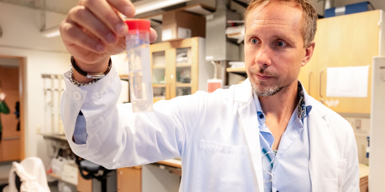 Johan Malmström håller upp ett provrör med röd kork i ett laboratorium.