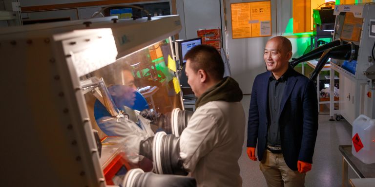 Två personer i ett laboratorium, en arbetar med skyddshandskar vid ett hölje.
