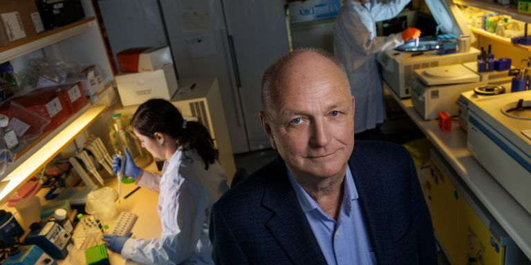 Forskningslaboratorium med en man i förgrunden och två personer som arbetar i bakgrunden.