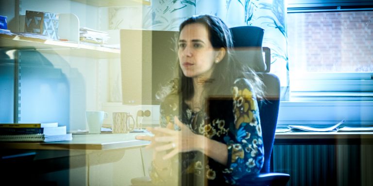 Kvinna sitter vid ett skrivbord och gestikulerar i ett kontorsutrymme.