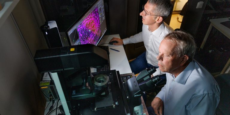 Jan Ellenberg och Mathias Uhlén vid ett mikroskop i ett laboratoriemiljö.