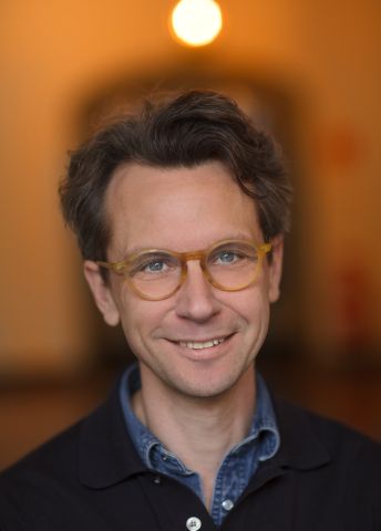 Leende man med glasögon, mjukt ljus i bakgrunden.