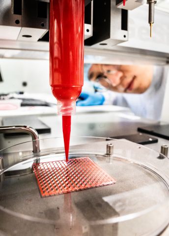 En röd vätska droppar från en pipett över ett rutmönstrat prov i ett laboratoriemiljö.