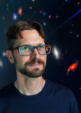Porträtt av man med glasögon, leende mot en stjärnig rymdbakgrund.