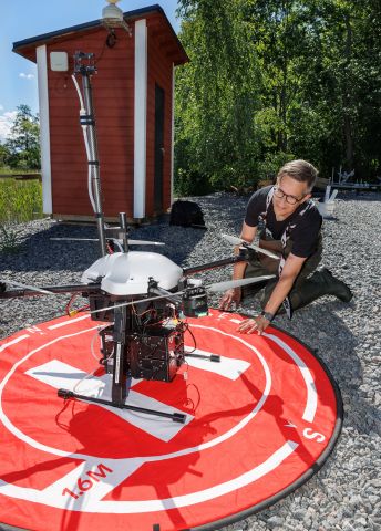 En person i arbetskläder förbereder en drönare på en röd landningsmatta.