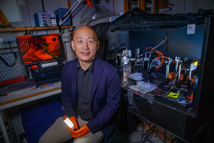 En man sitter framför vitvaror i ett laboratoriemiljö, håller i en lampa.