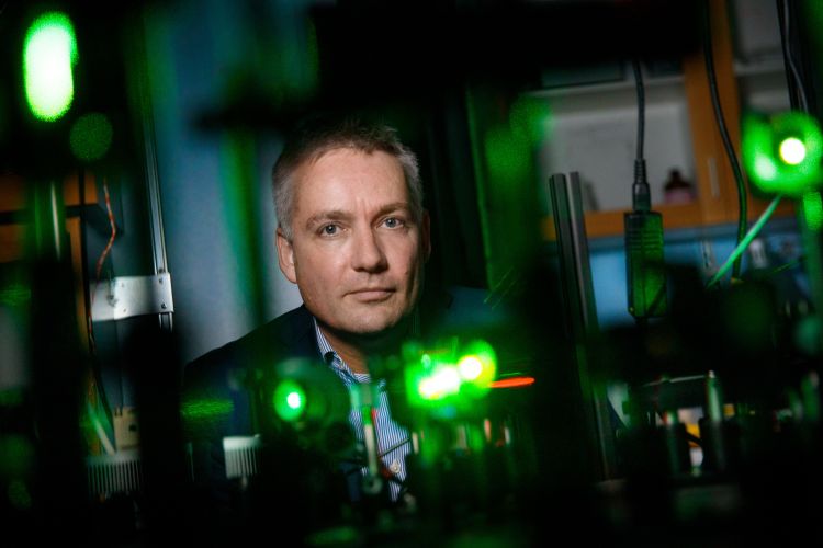 En man står framför en laboratoriemiljö med gröna ljus och optisk utrustning.