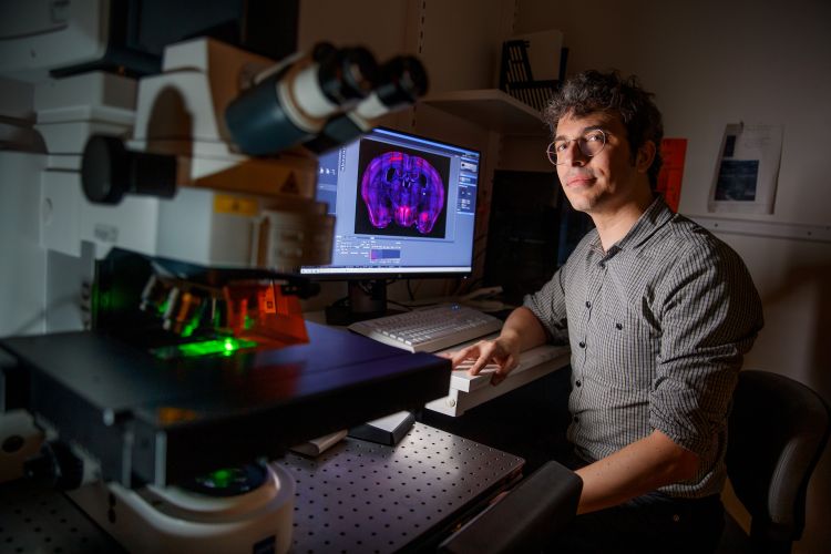 En man sitter vid en dator med en mikroskop i förgrunden, omgiven av forskningsutrustning.