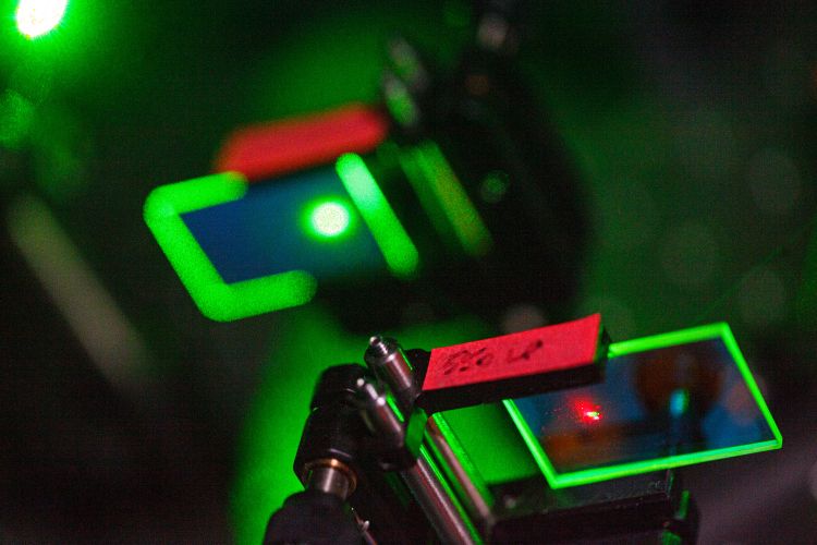 Gröna laserstrålar reflekteras genom små färgade filter i en laboratoriemiljö.