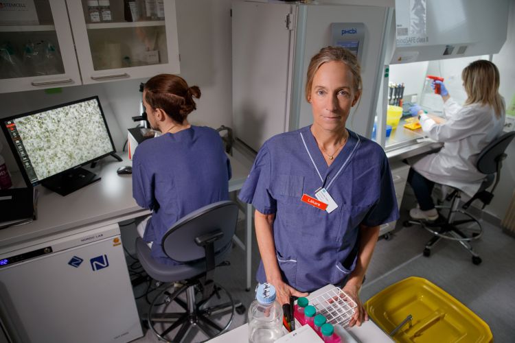 Kvinna i laboratoriemiljö håller en provplatta, andra forskare arbetar i bakgrunden.