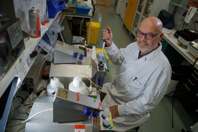 En man i labbrock arbetar med pipetter i ett laboratorium.