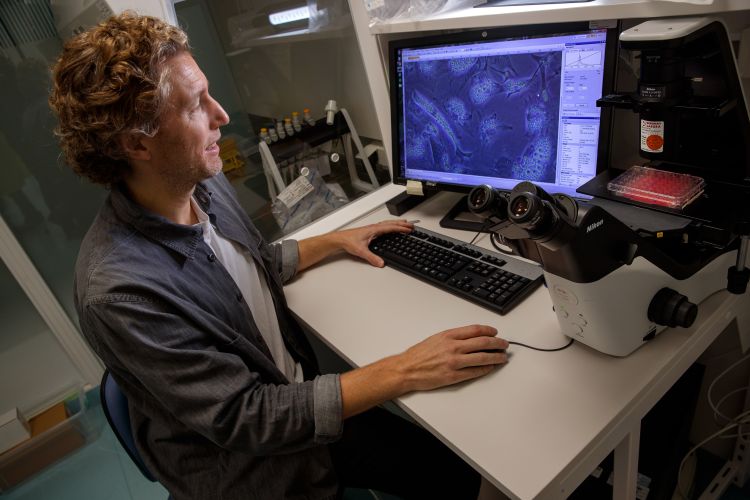 Man i laboratorium arbetar vid en dator med mikroskop och prover i bakgrunden.