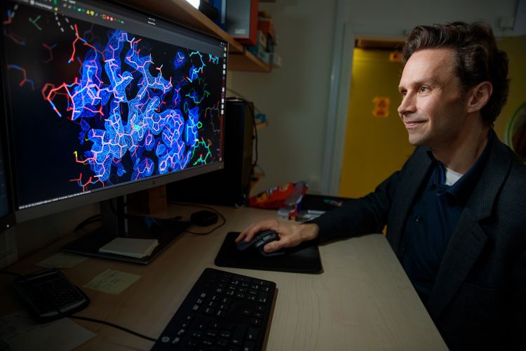 En man arbetar vid en dator med en färgglad molekylärstruktur på skärmen.