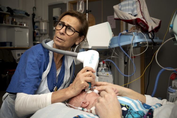 Sjuksköterska vårdar en nyfödd med medicinskt utrustning i ett sjukhusrum.