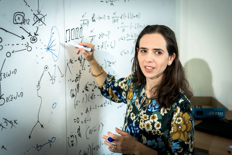 Kvinna skriver på en vit tavla täckt med matematiska formler och diagram.