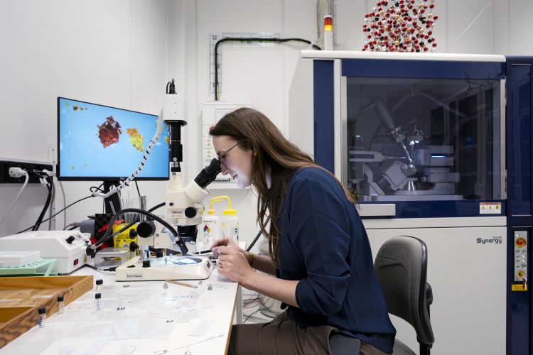 Kvinna som arbetar vid mikroskop i ett laboratorium med en datorskärm i bakgrunden.