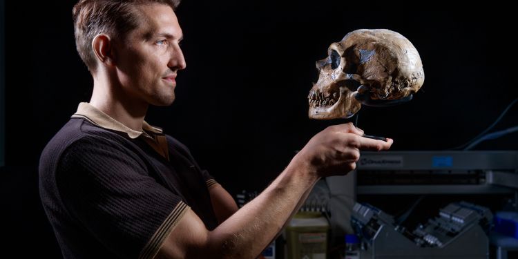 En man som håller en mänsklig skalle i en laboratoriemiljö.