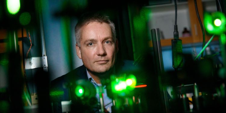 En man står framför en laboratoriemiljö med gröna ljus och optisk utrustning.